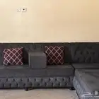 كنب متصل واسع لونه رمادي فحمي معاه أربع مراكي وثمان مخاد